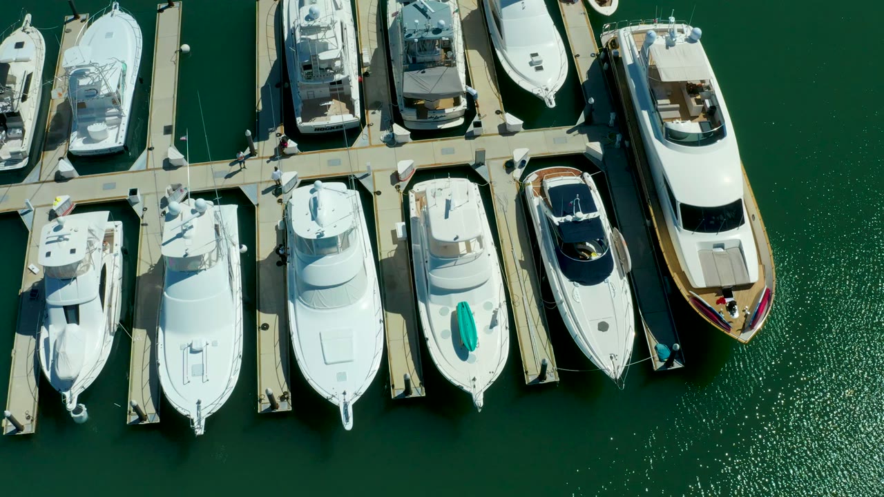 Top-down marina slips with white yachts and sunlit green water.