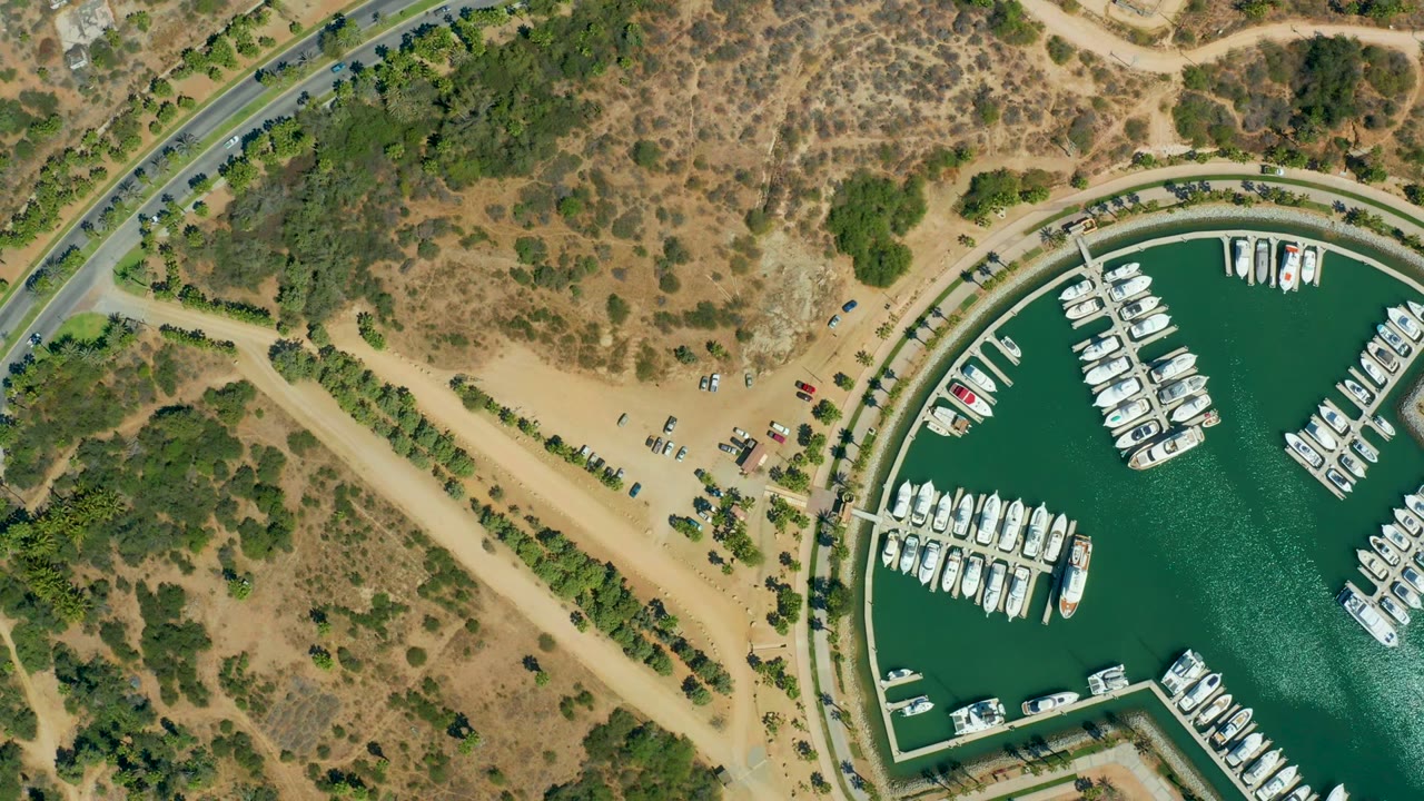 Aerial marina basin with docks, boats, cars, roads, and scrubby land