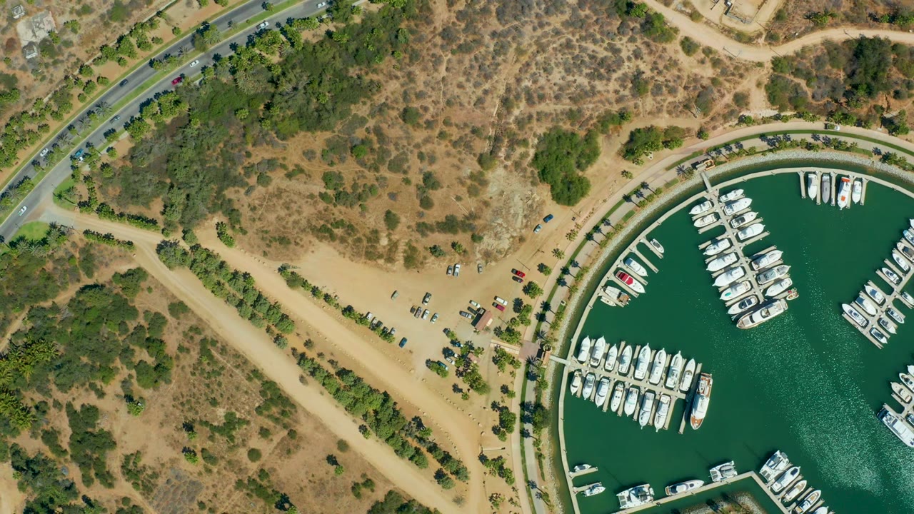 Aerial marina and curved road with parked boats and small vehicles nearby.