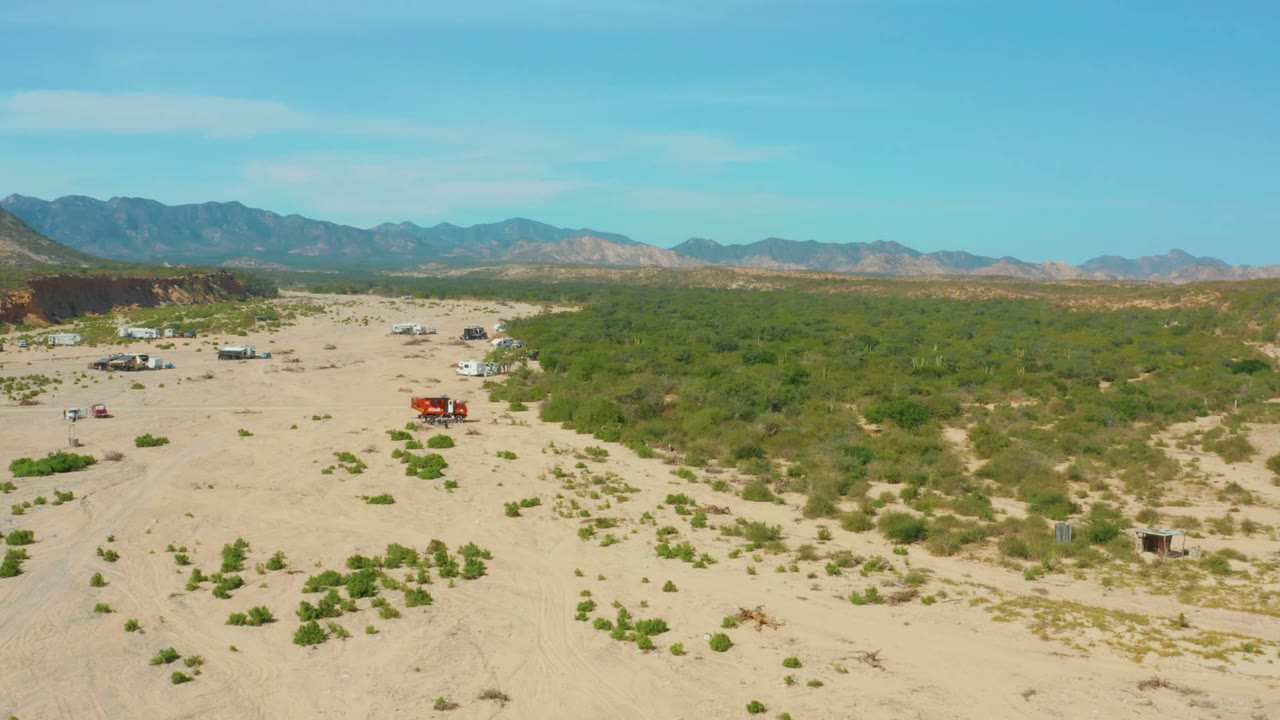 Wide aerial desert scene with red truck and white trailer near shrubs