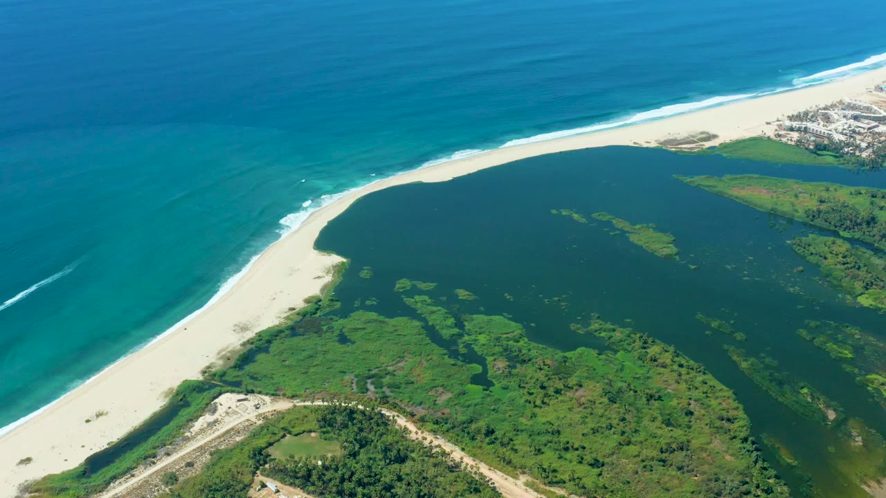 Aerial coastline with white sand between turquoise ocean and dark lagoon water.