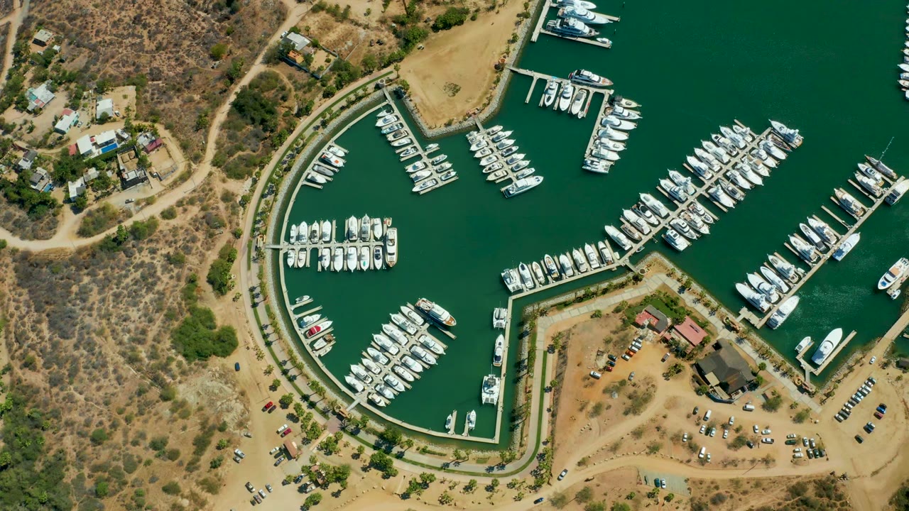 Aerial view of marina docks with many white boats and dry land around the basin.