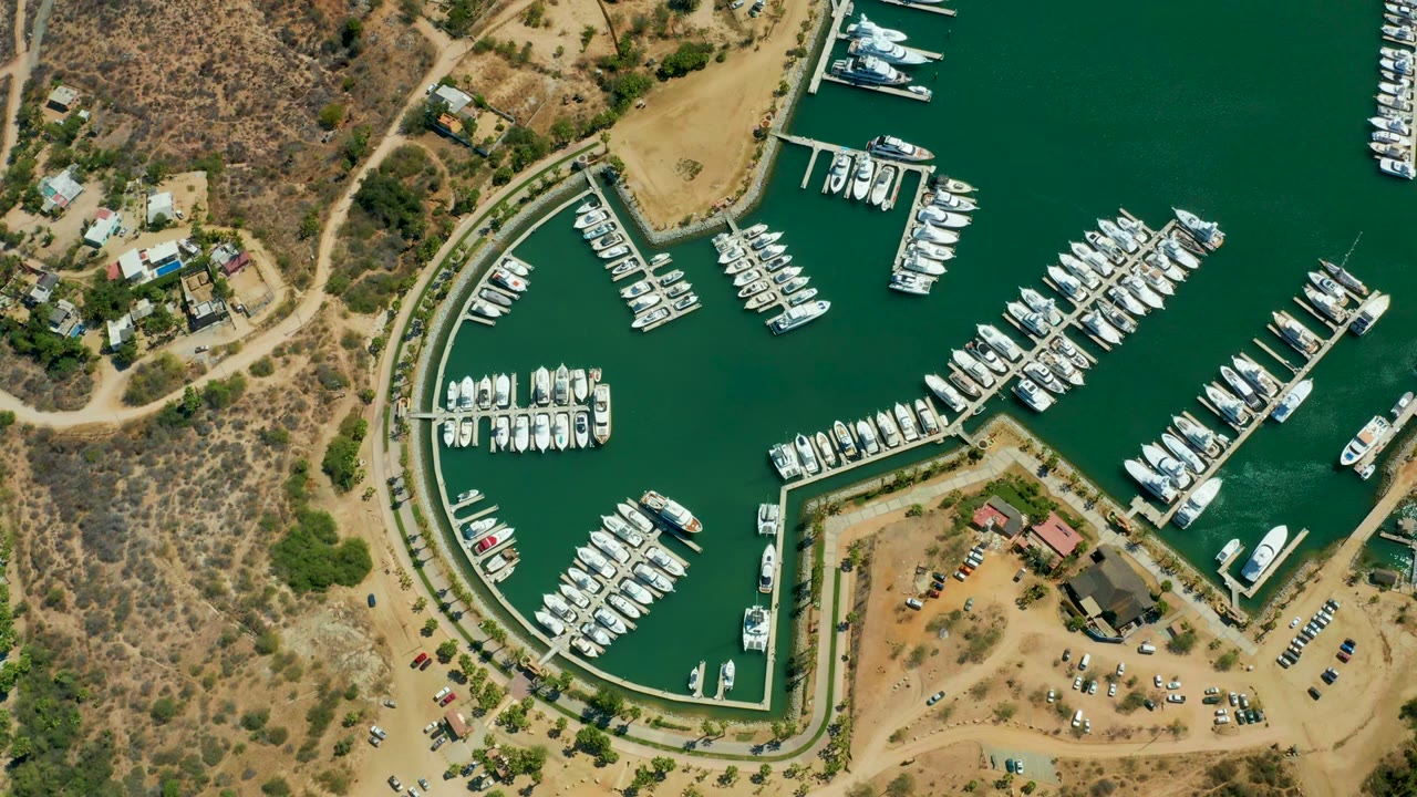Aerial marina basin with rows of boats and docks beside dry shoreline terrain.