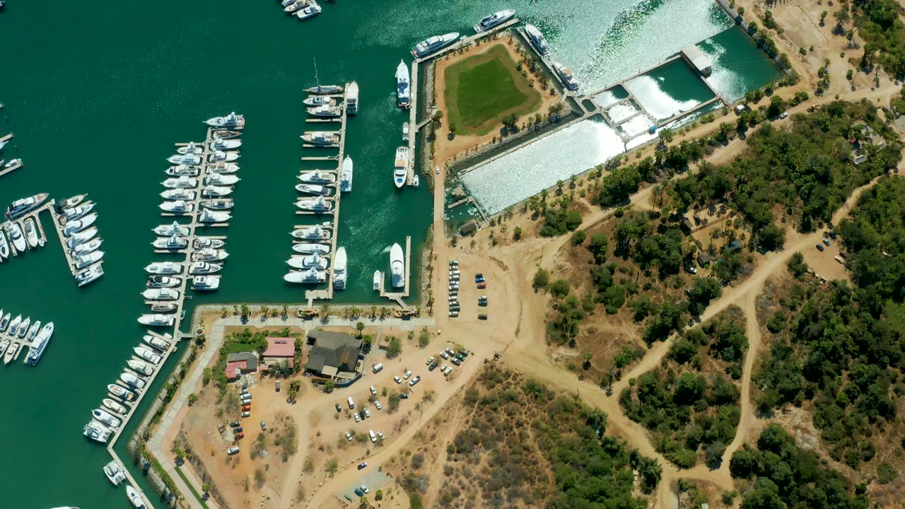 Aerial marina view with white boats along docks and a vessel near the dock entrance.