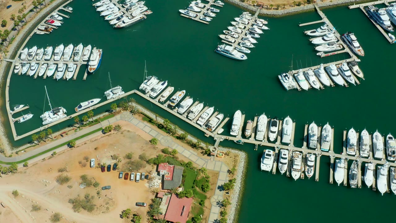 Aerial marina view with white boats around docks and sandy shoreline below.