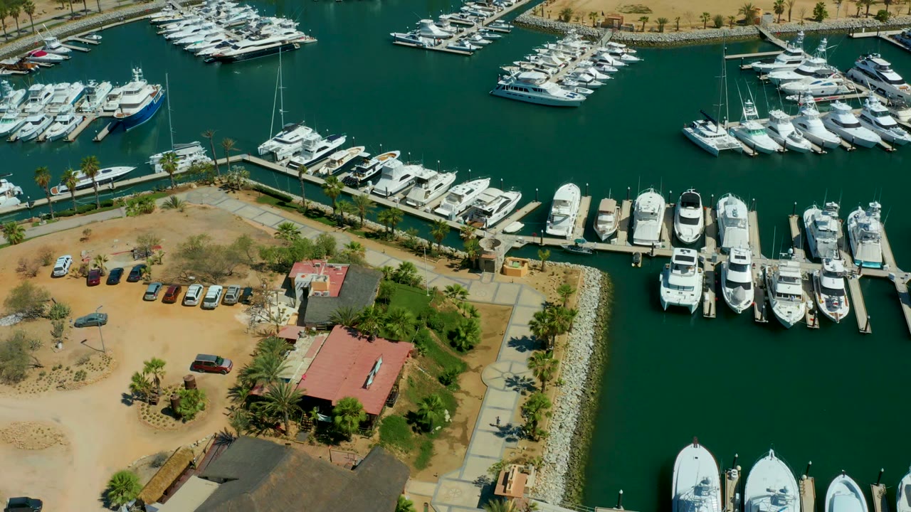 Aerial marina view with clustered yachts and a red-roofed waterfront building.
