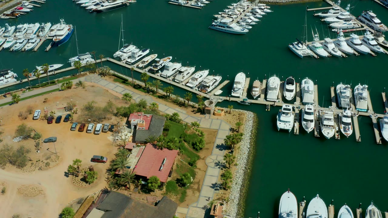 Overhead marina frame with yachts, docks, parked cars, and red-roofed buildings.