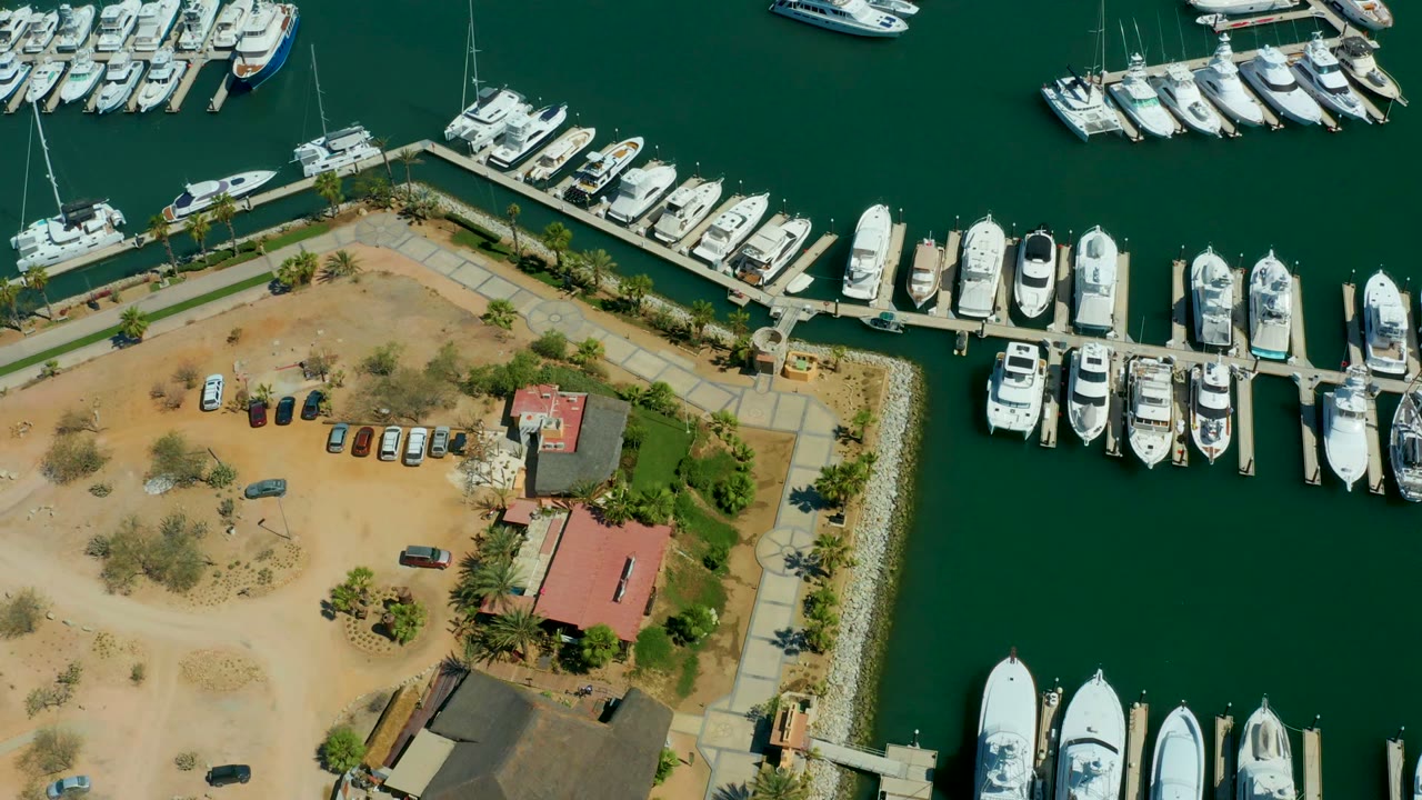 Aerial view of boats docked around green marina water and adjacent cars.