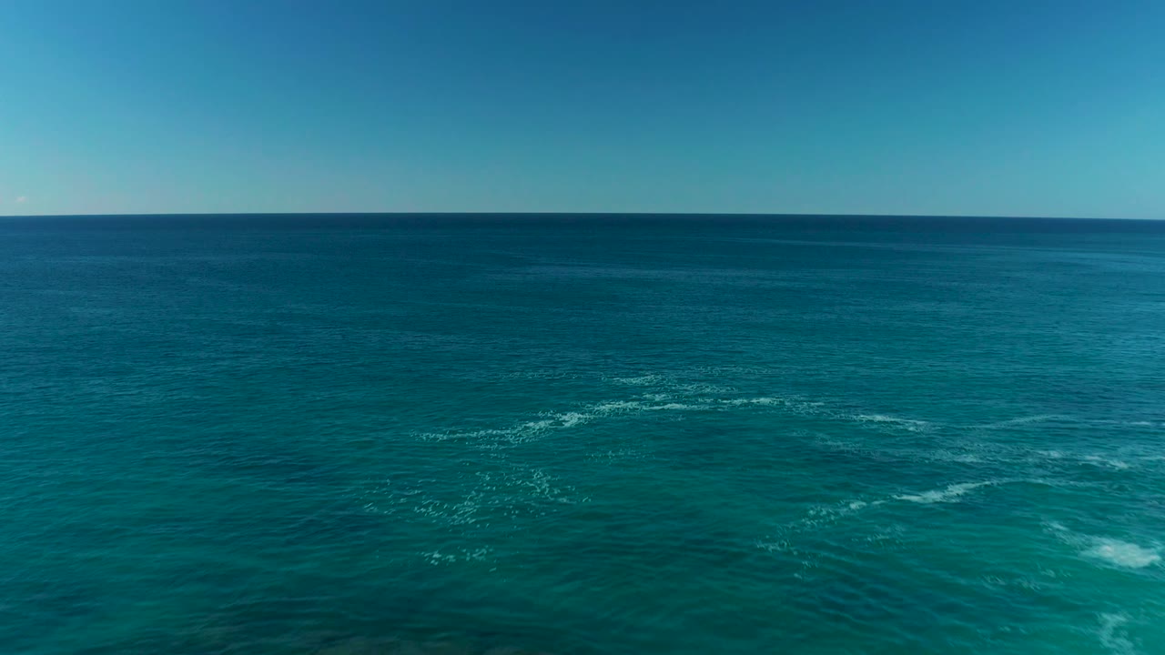 Aerial view over turquoise ocean near La Fortuna, Baja California Sur, with scattered white foam below a clear horizon and no visible people.