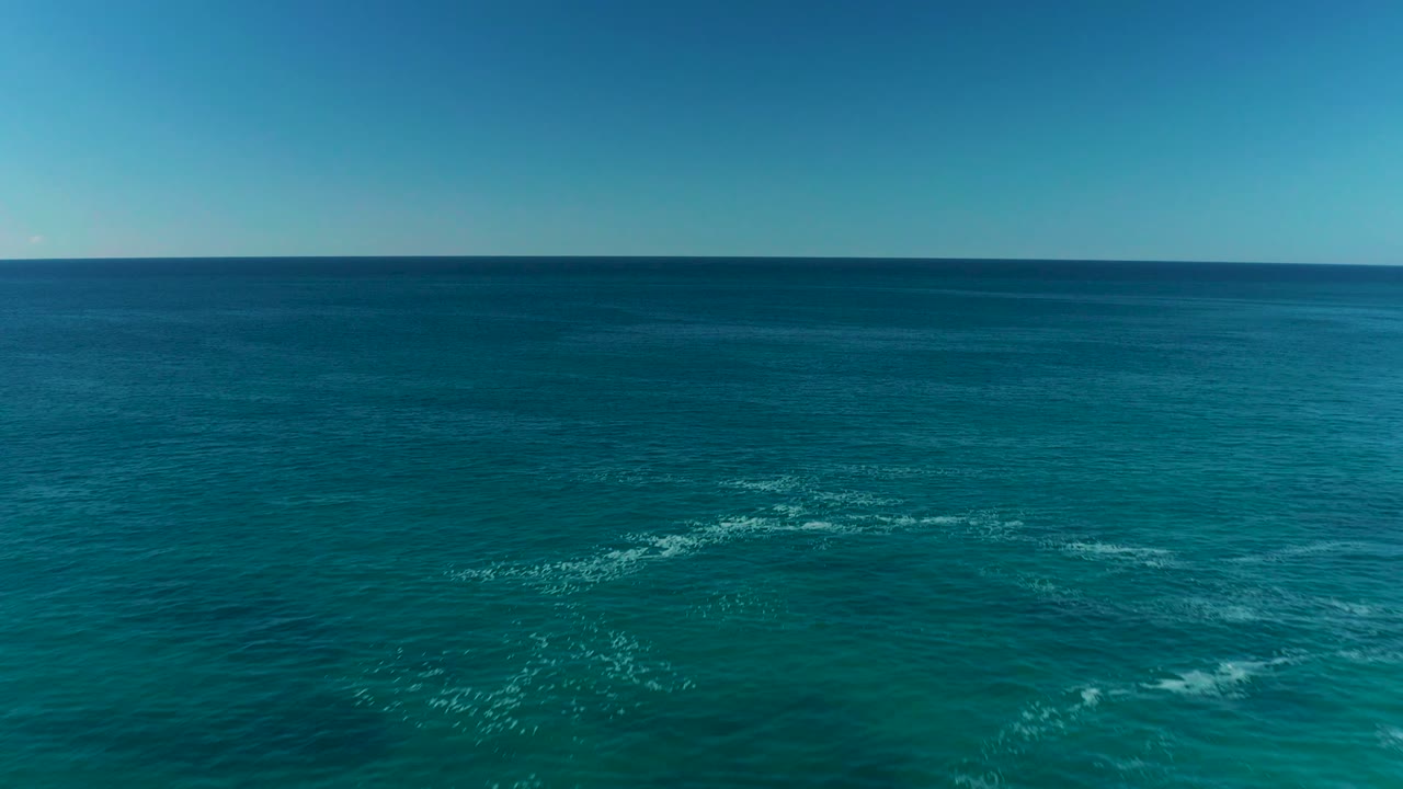 Blue ocean with thin white foam streaks under clear sky