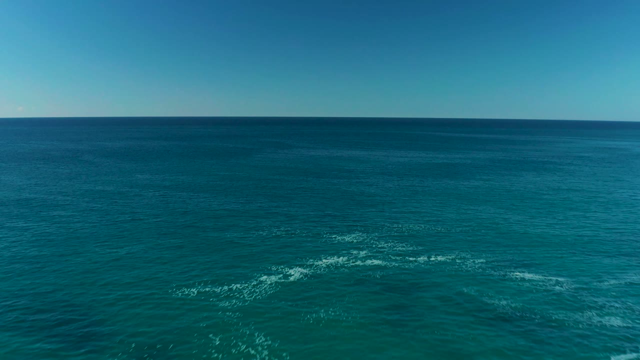Aerial view of open turquoise water near La Fortuna with white foam patches spread across the midground, clear blue sky, and no visible people.