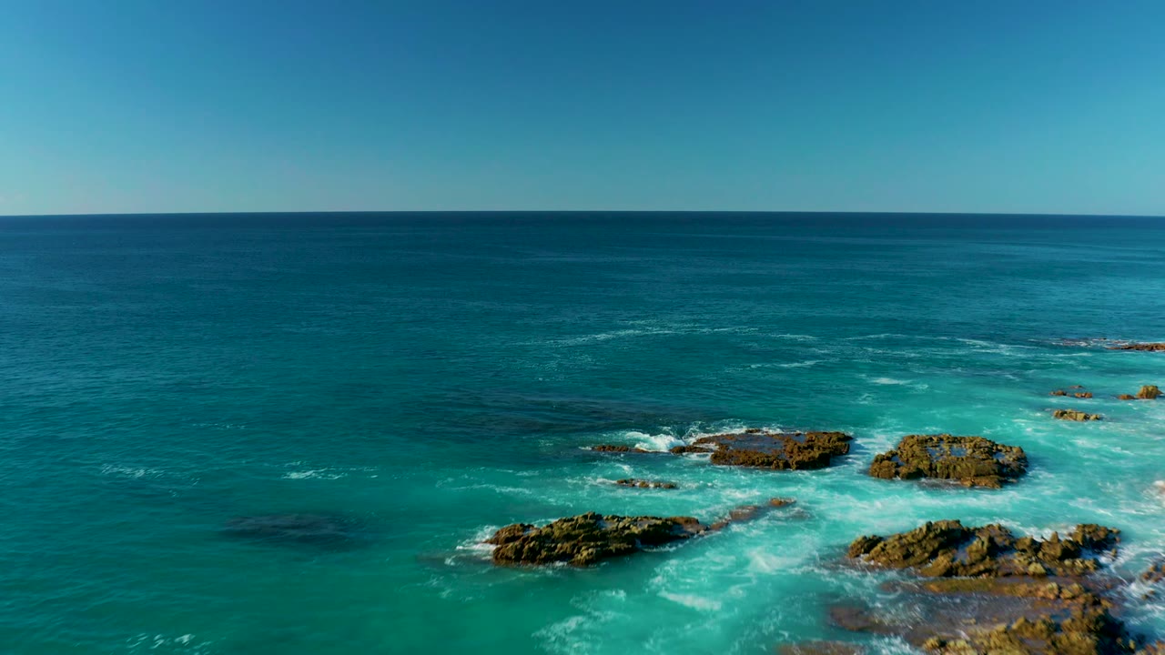 Aerial frame at La Fortuna, Baja California Sur, showing rocky outcrops more centered in turquoise water with deep blue sea beyond and no visible people.