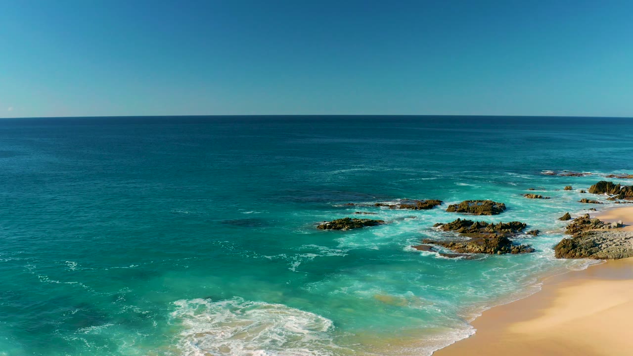 White surf circling rocky outcrops in clear blue-green water.
