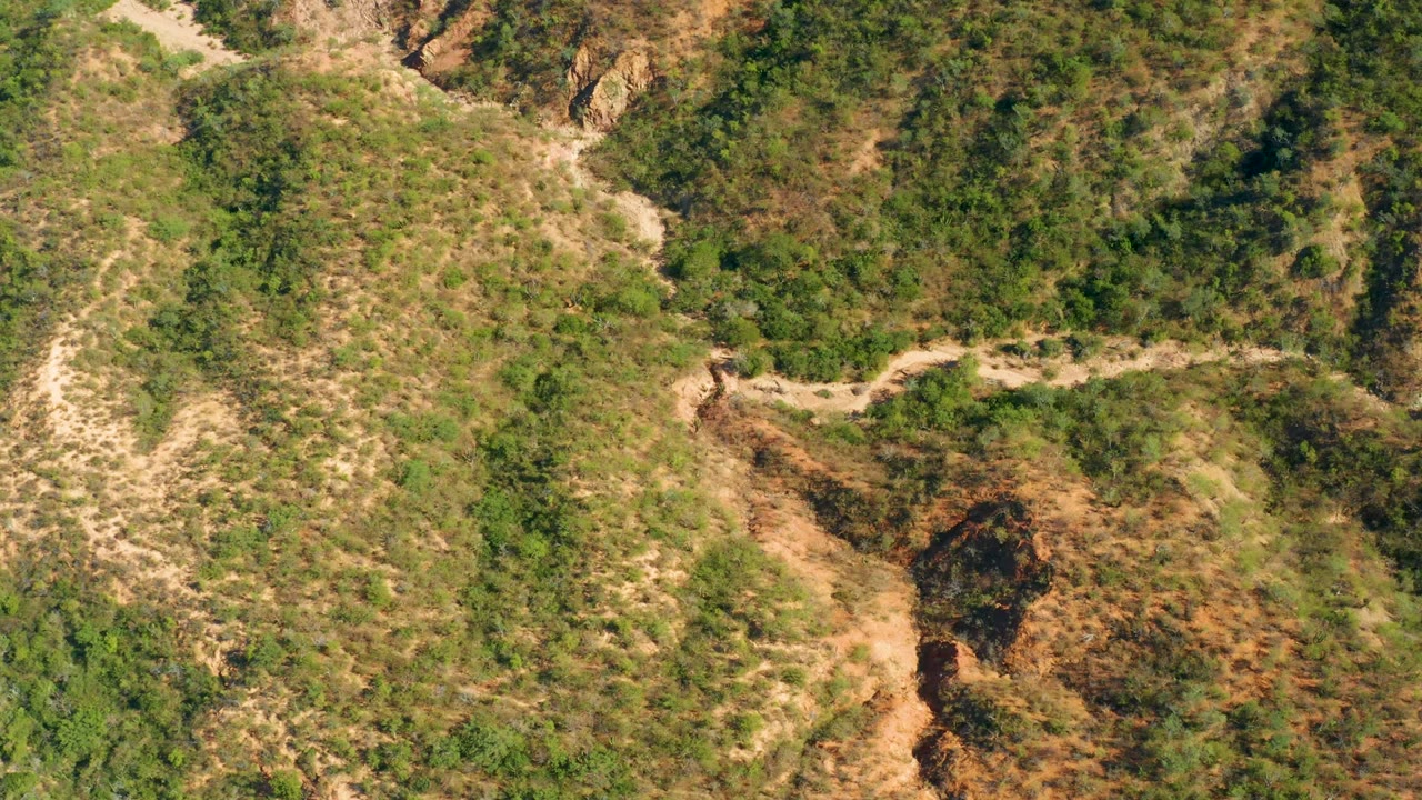 Dirt track curves along a scrubby hillside with an eroded gully below.