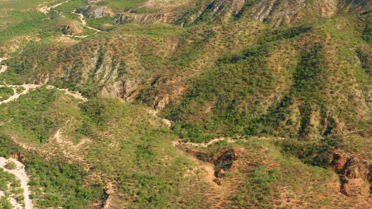 Aerial frame from El Salado Viejo, Los Cabos showing scrub-covered hills, exposed dry slopes, and a pale winding dirt road at the lower left, with no visible people.