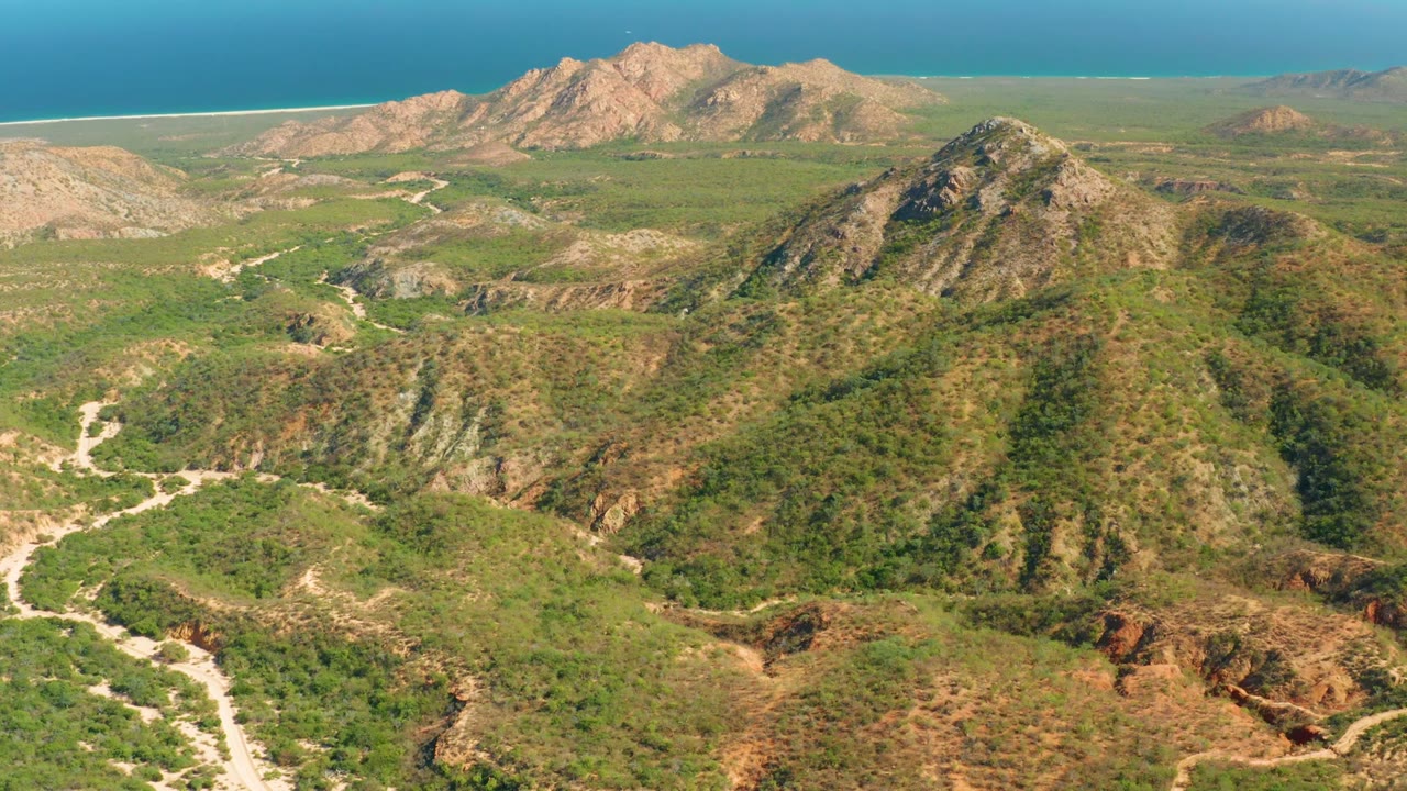 Coastal mountains with a central green ridge, winding dirt paths, and ocean beyond.