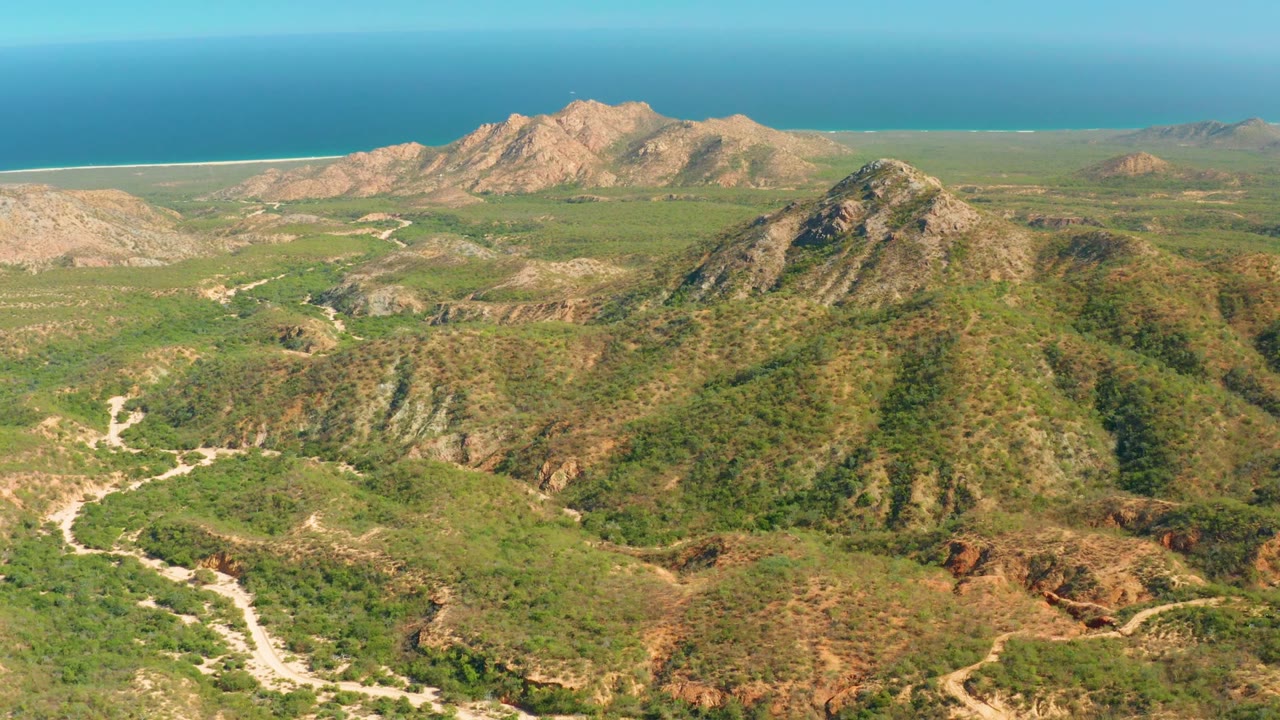 High view across rocky green hills with a winding road and ocean horizon.