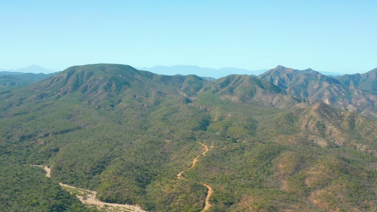 Wide aerial mountain landscape with dirt road curves across green slopes.