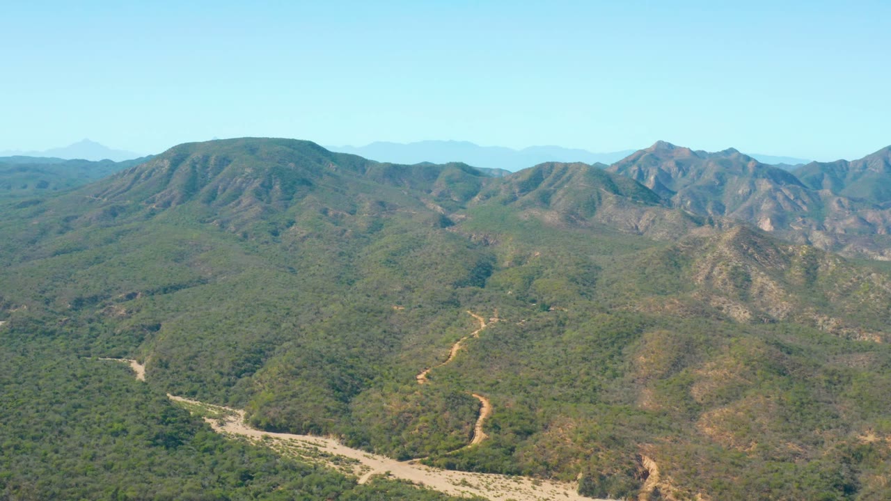 Aerial mountain valley with ridges, dry vegetation, and a winding wash.