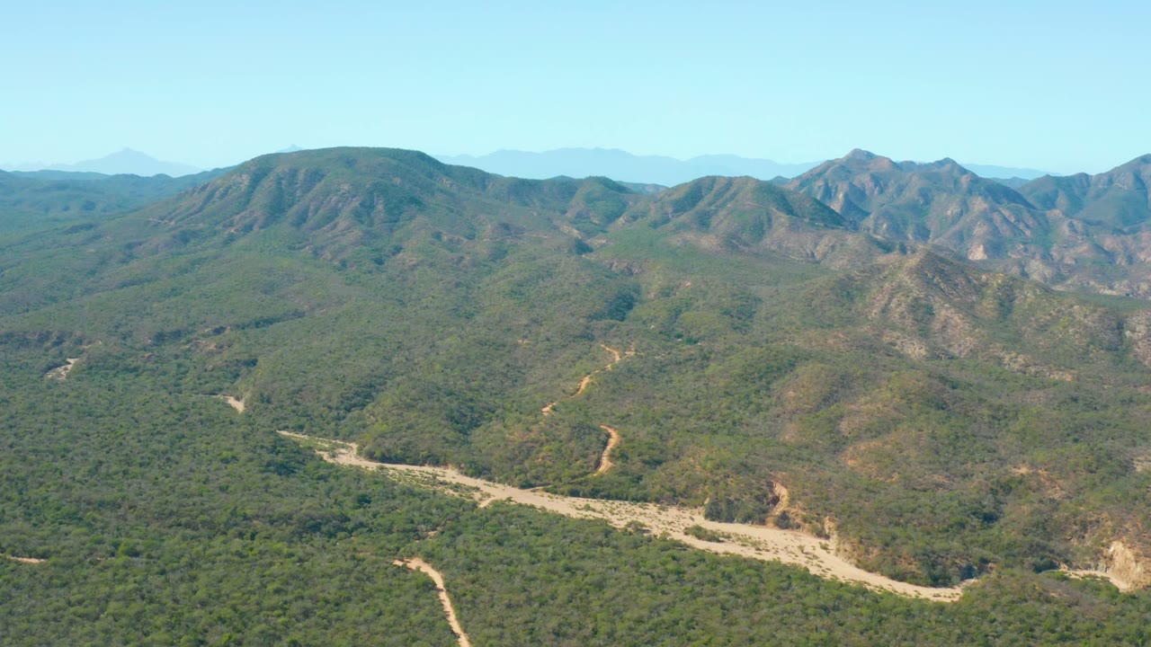 Forested valley with a winding pale stream channel below layered mountain ridges.