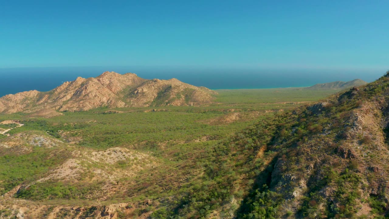 Rocky mountain range above a green valley with ocean on the horizon.