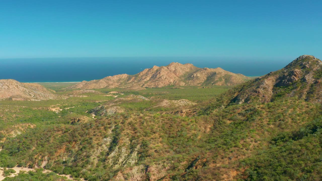 Third frame over El Salado Viejo Los Cabos, showing layered green-brown hills in the foreground, tan mountain peaks across the middle, ocean beyond, and no visible people.