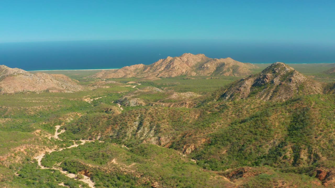 Frame 0:02 shows El Salado Viejo Los Cabos from above, with scrub-covered hills, pale road curves, rocky mountain forms, blue ocean in the background, and no visible people.
