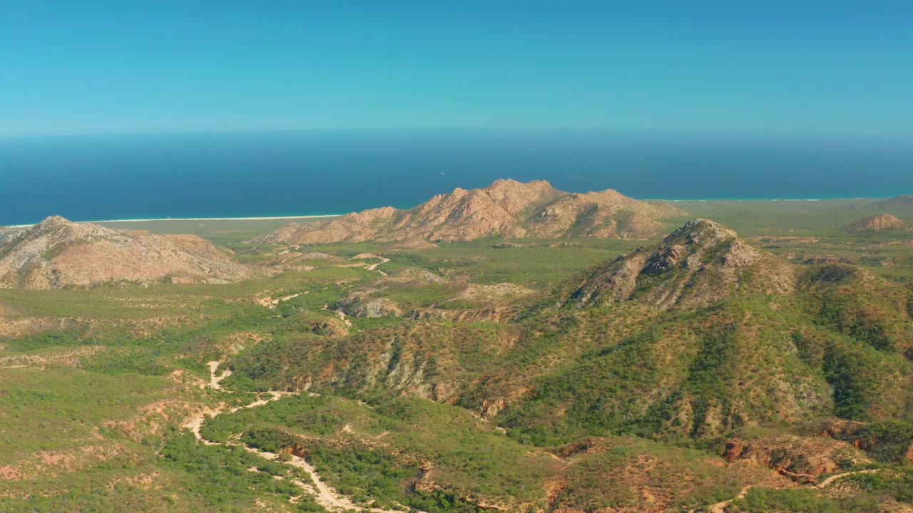 Green valley road below rocky hills and distant blue ocean