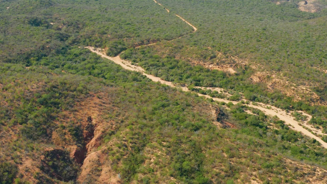 Winding dirt road crossing scrub-covered hills from an aerial angle.