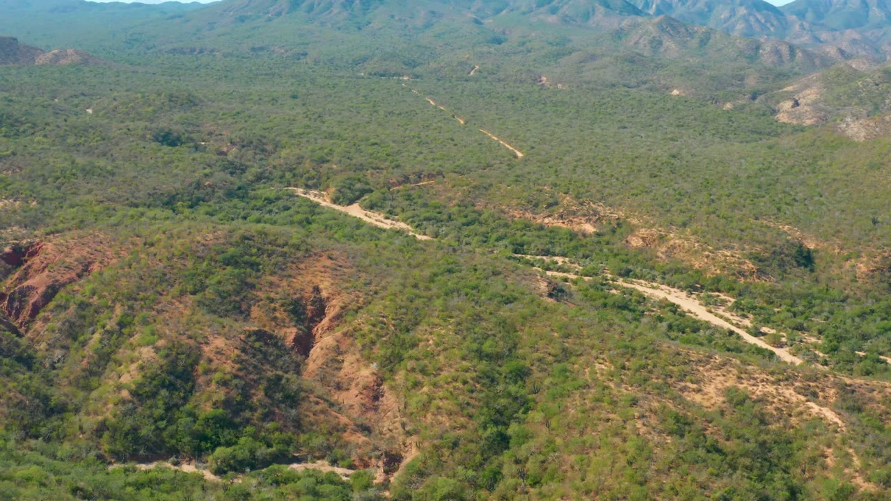 Wide aerial landscape with dirt road curving across scrub-covered hills