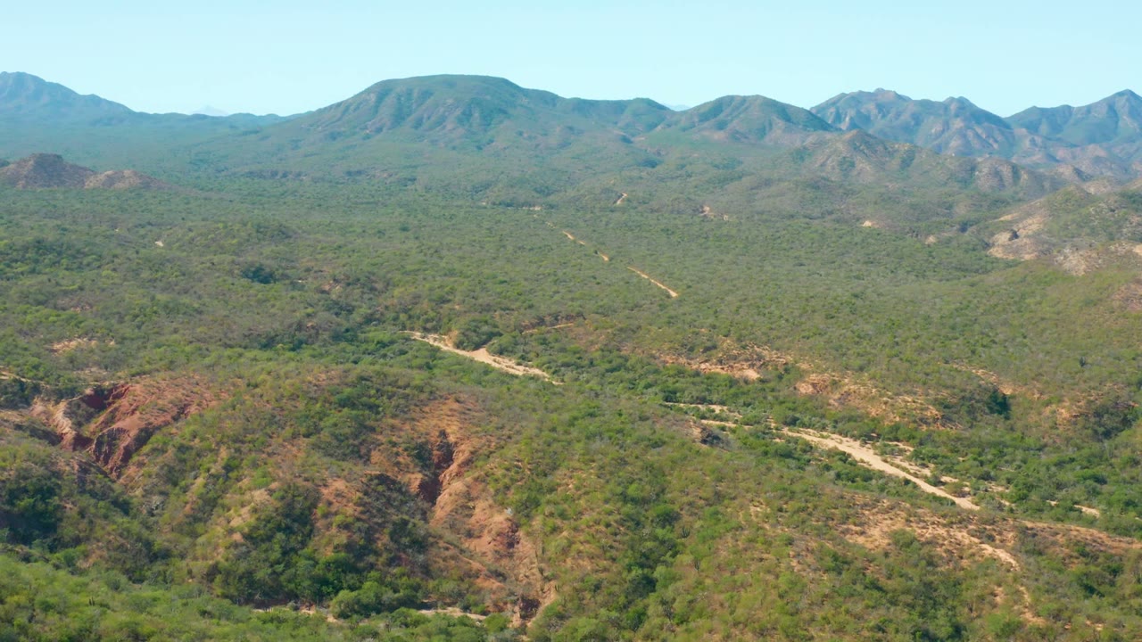 Wide aerial landscape with a dirt road cutting through green mountainous terrain.