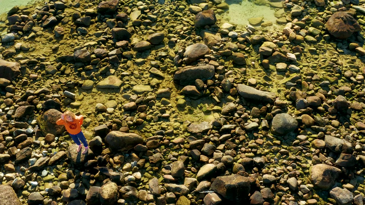 Person in orange stepping across shallow rocky water