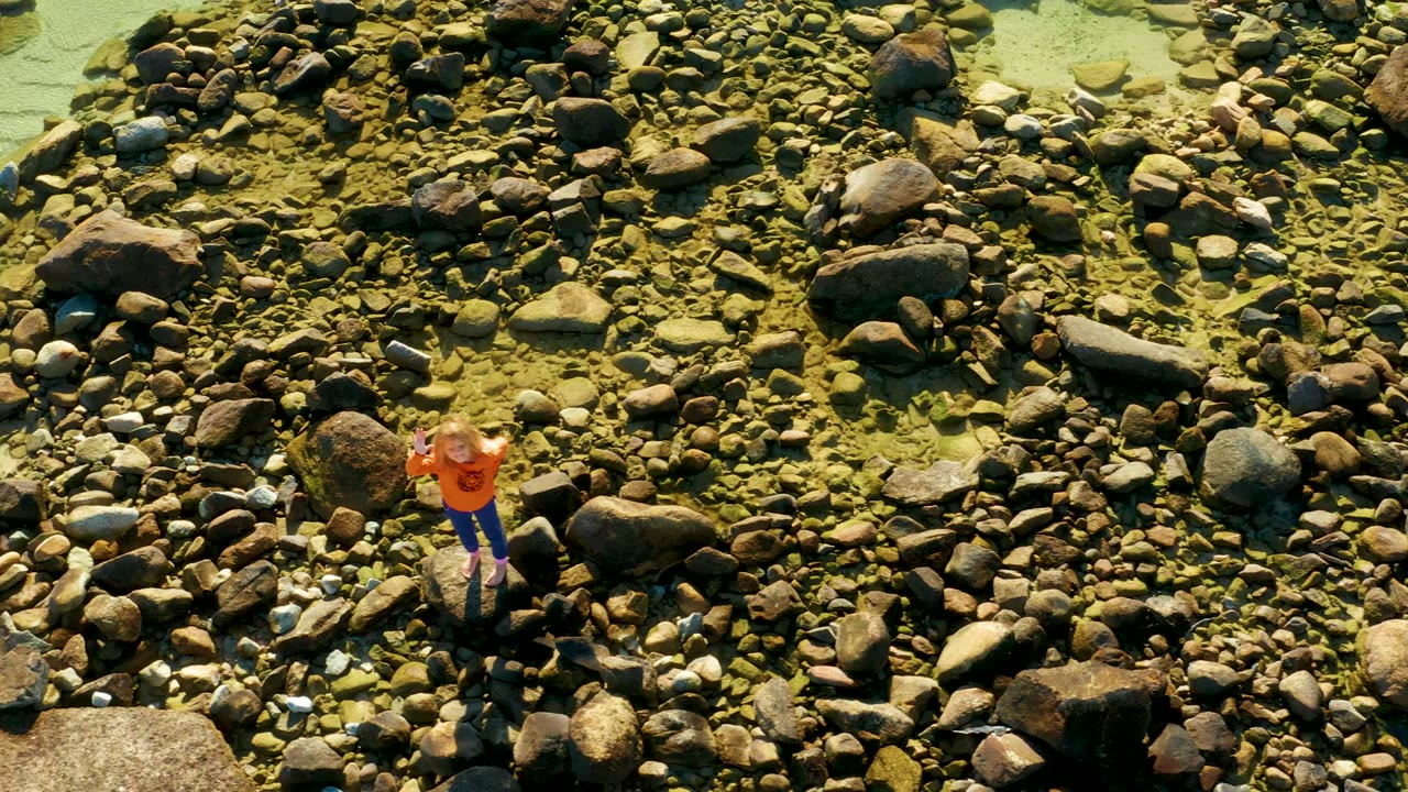 At 0:02, the aerial frame holds the person near the center of the El Tule river rocks, with large boulders and smaller pebbles filling the view.