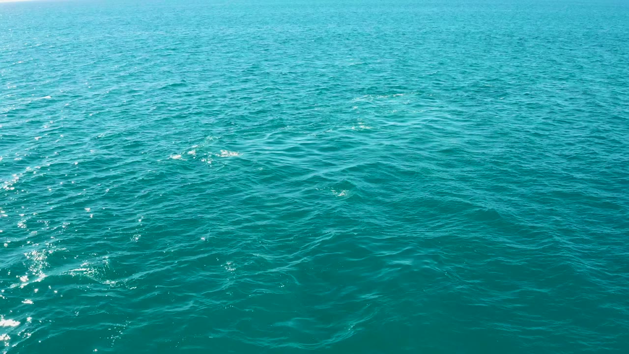 Turquoise ocean surface at El Tule Los Cabos with small ripples, bright reflections near the left edge, a faint horizon band, and no visible people.