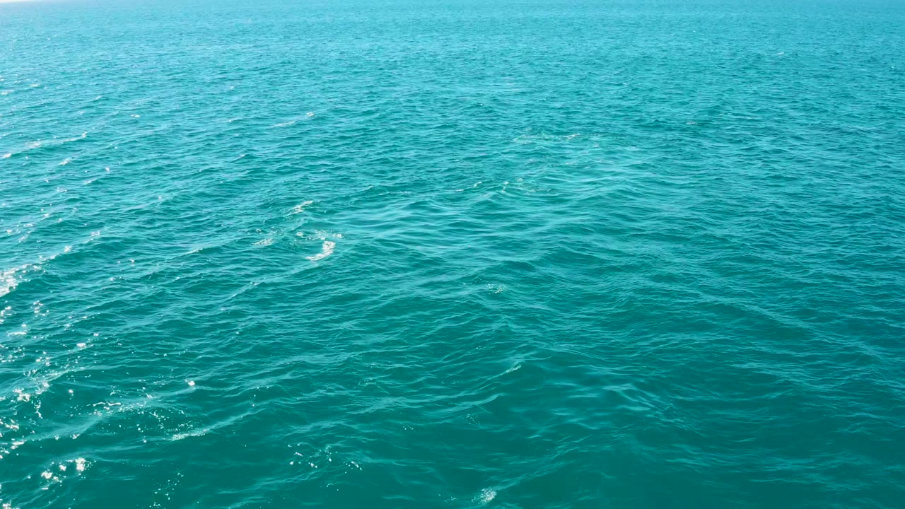 Turquoise sea surface at El Tule Los Cabos shows diagonal streaks of white foam and rippled water under bright light, with no visible people.