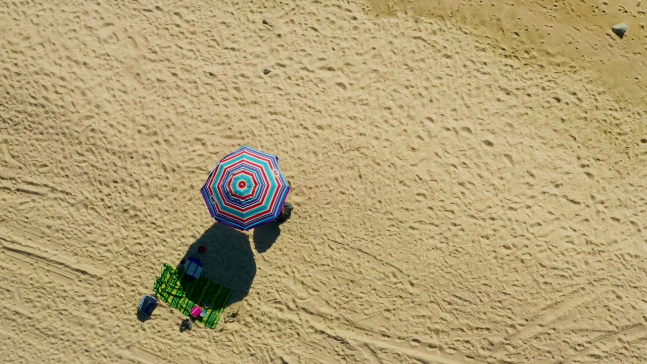 Striped umbrella casting a dark shadow beside a green beach chair.