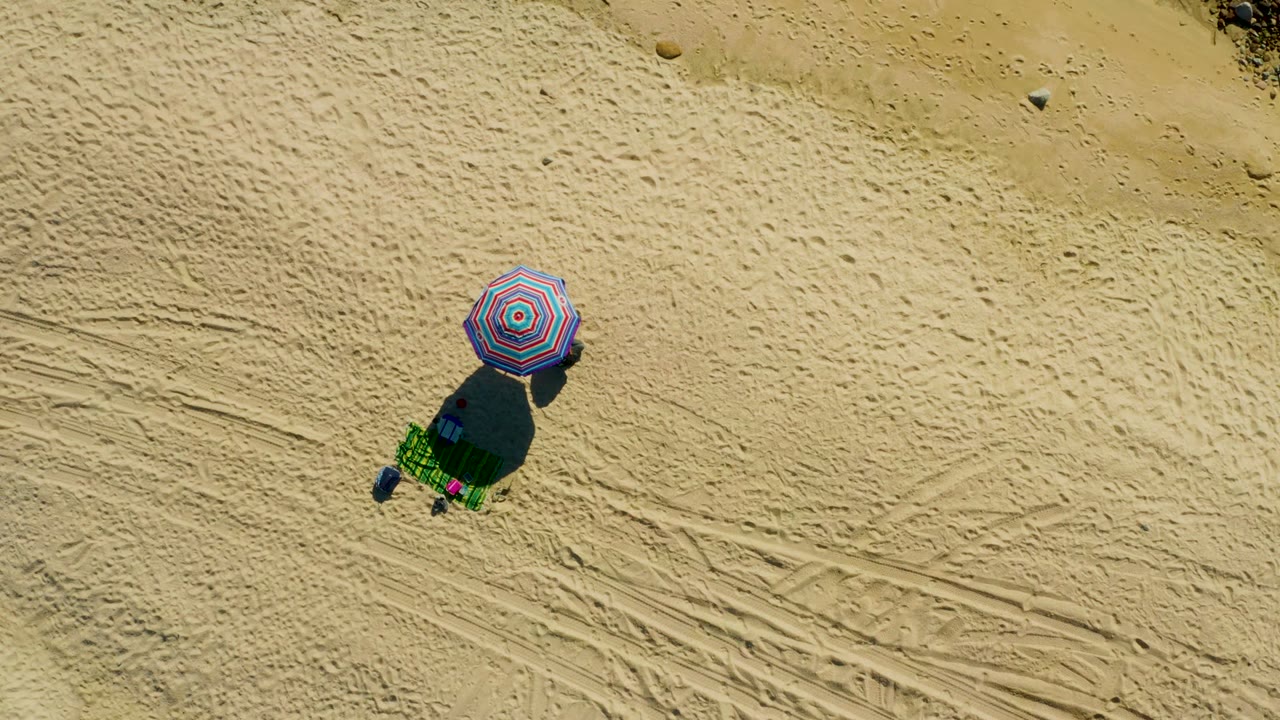 Striped umbrella and green chair casting a shadow on sand