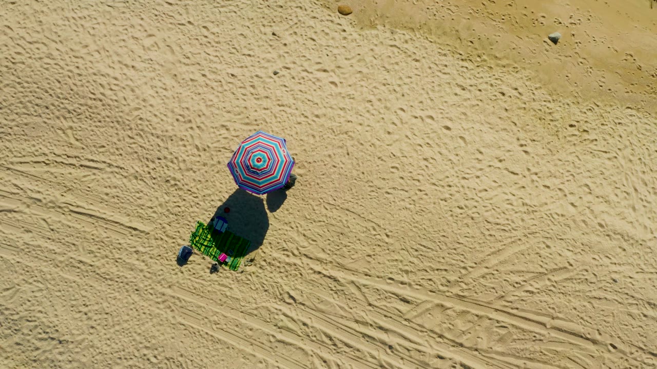 Top-down beach umbrella and chair beside tire marks