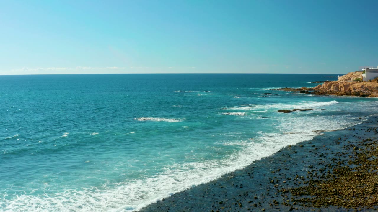 Foamy waves spread across rocks with turquoise water and a headland at right.