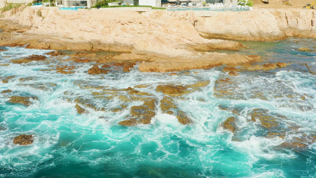 Foamy ocean waves washing across rocks near a pale cliff.