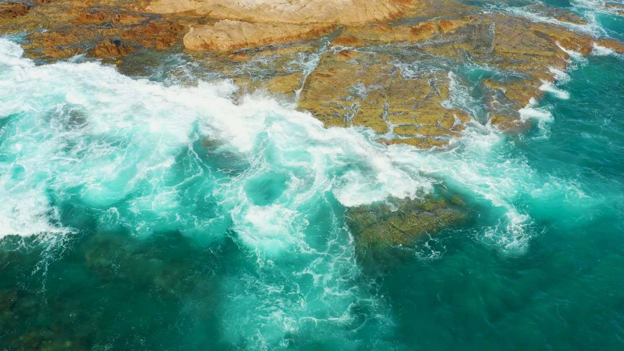 Turquoise water breaks into white foam over brown rock shelves at Chileno Beach in Los Cabos, with no visible people.