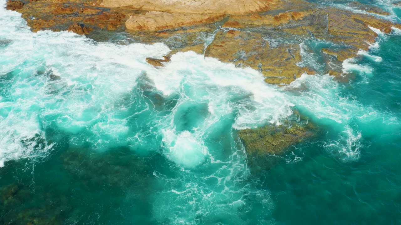 Whitewater spreads across a rocky ocean edge.