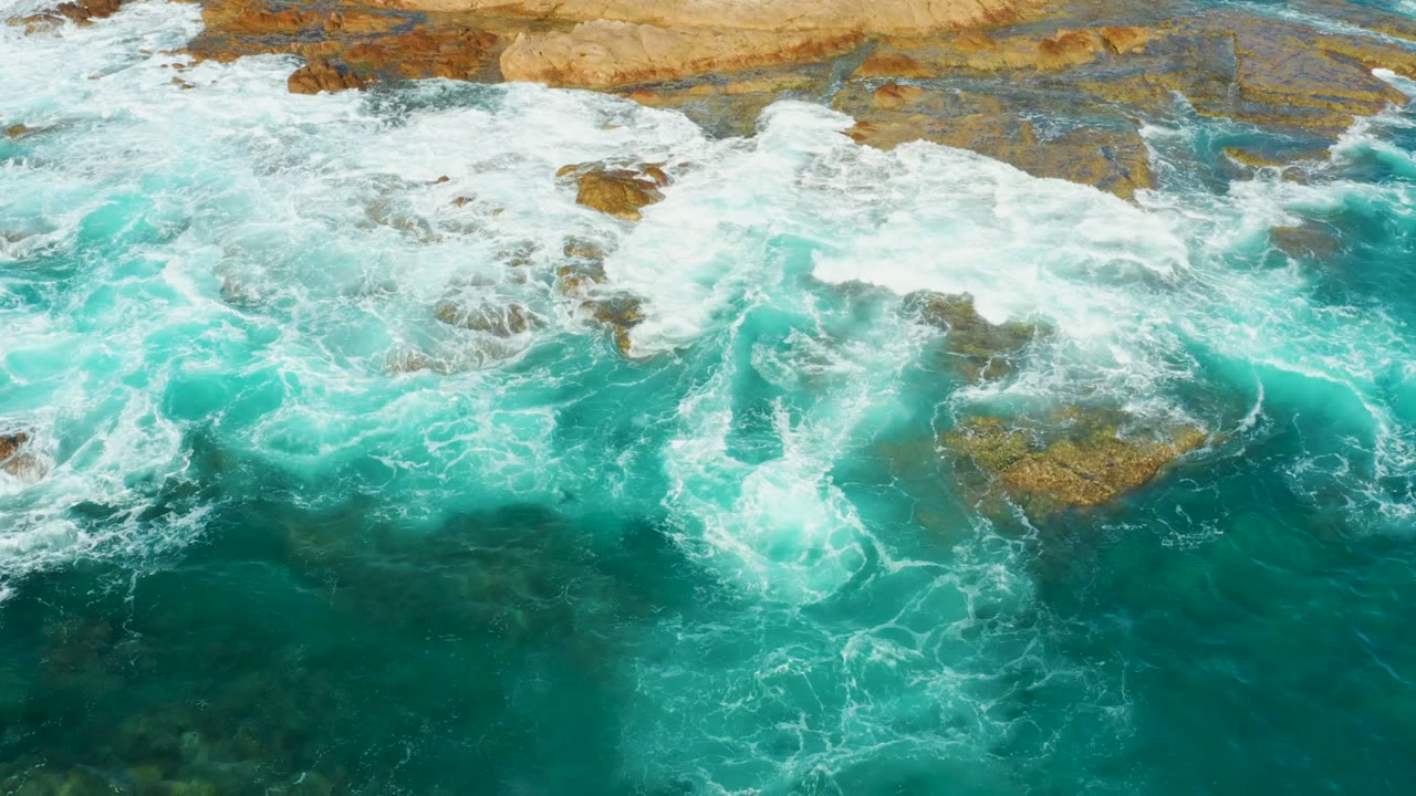 Aerial view of waves washing over uneven rocks.