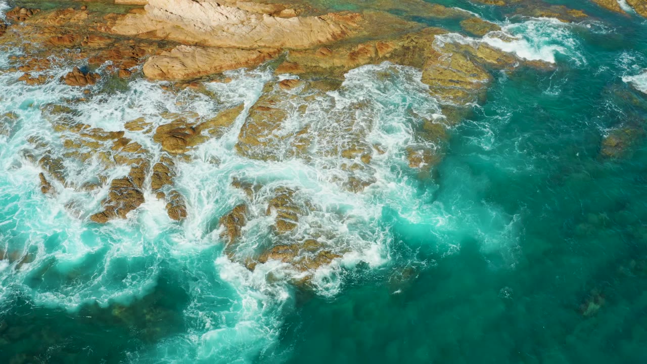 Overhead frame at Chileno Beach Los Cabos shows turquoise water and white foam crossing brown rock shelves, with no visible people.