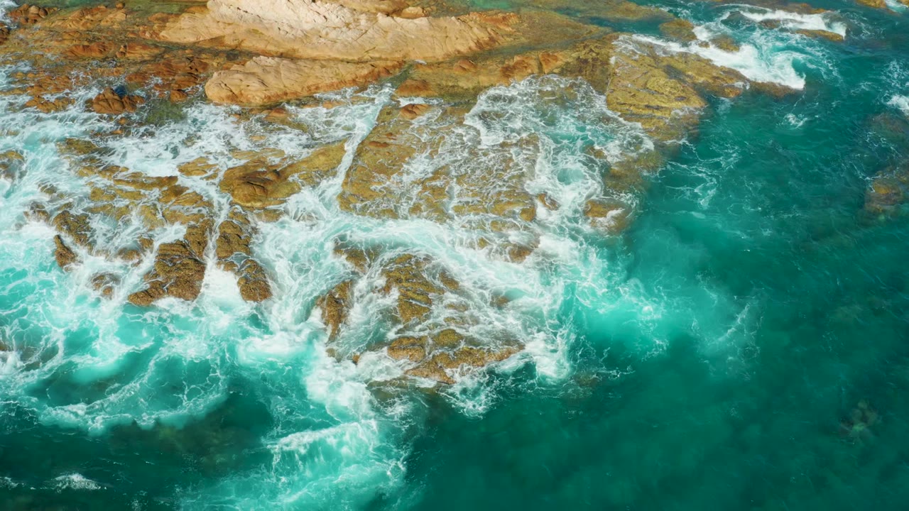 White surf spreading across jagged rocks in turquoise water
