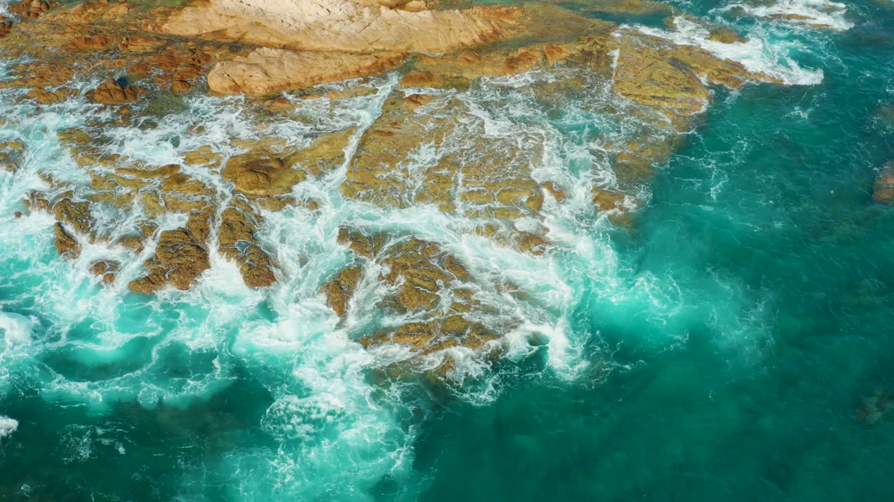At 0:02, the foamy wave pattern wraps around the central rocks at Chileno Beach Los Cabos, leaving clearer turquoise water along the right side, with no visible people.