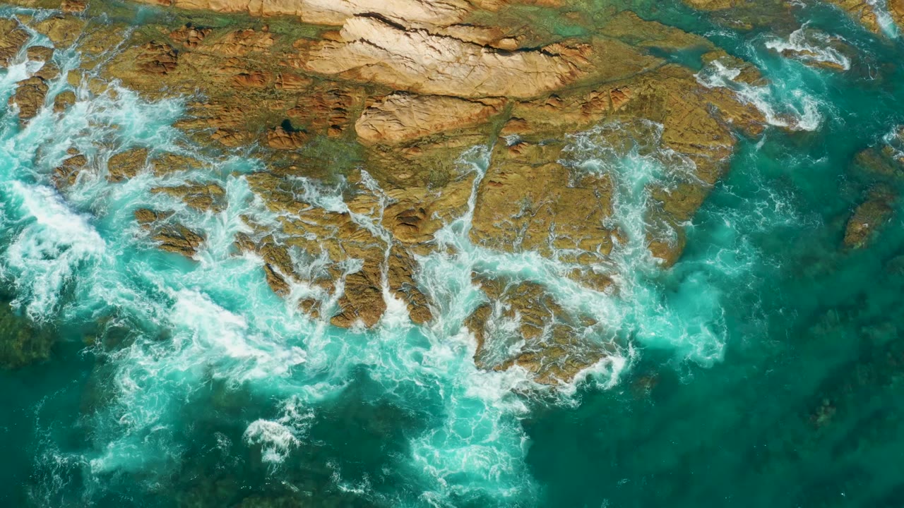 Whitewater expands around rocky shelves in clear turquoise water.