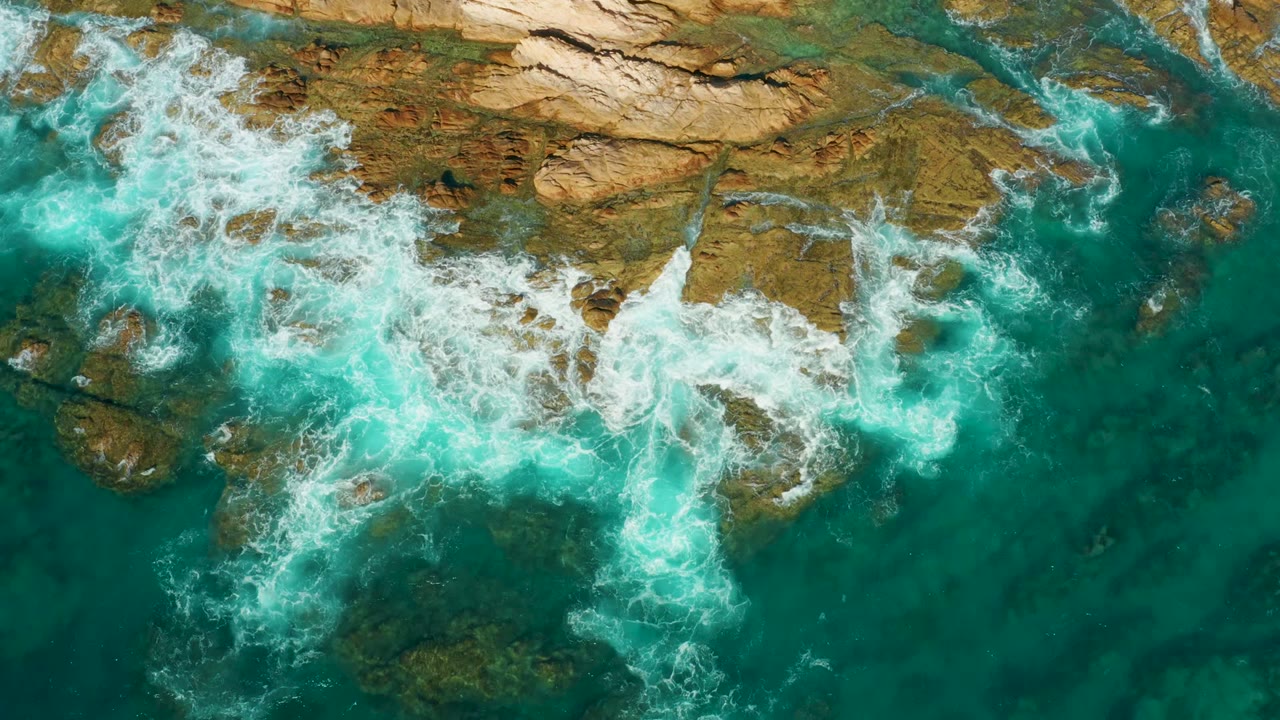 White foam spreads over submerged rocks in clear green-blue water.