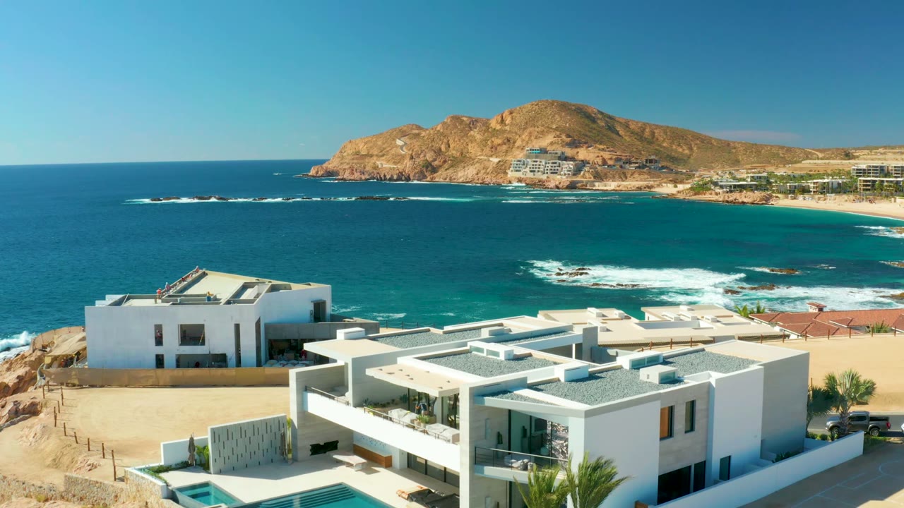 Modern white buildings and pool above turquoise water and surf.