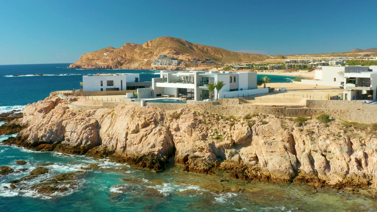 Modern white homes above rocky coastline and turquoise surf.